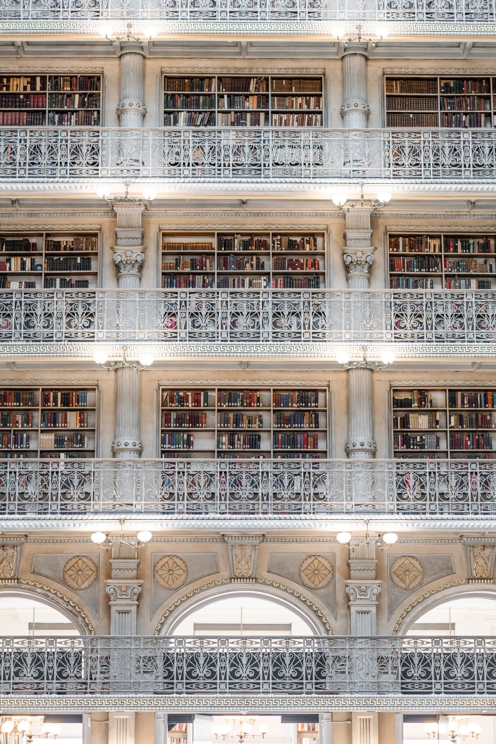 A grand library interior with four levels of book-filled balconies, adorned with ornate white railings and warm lighting, exuding a serene atmosphere.