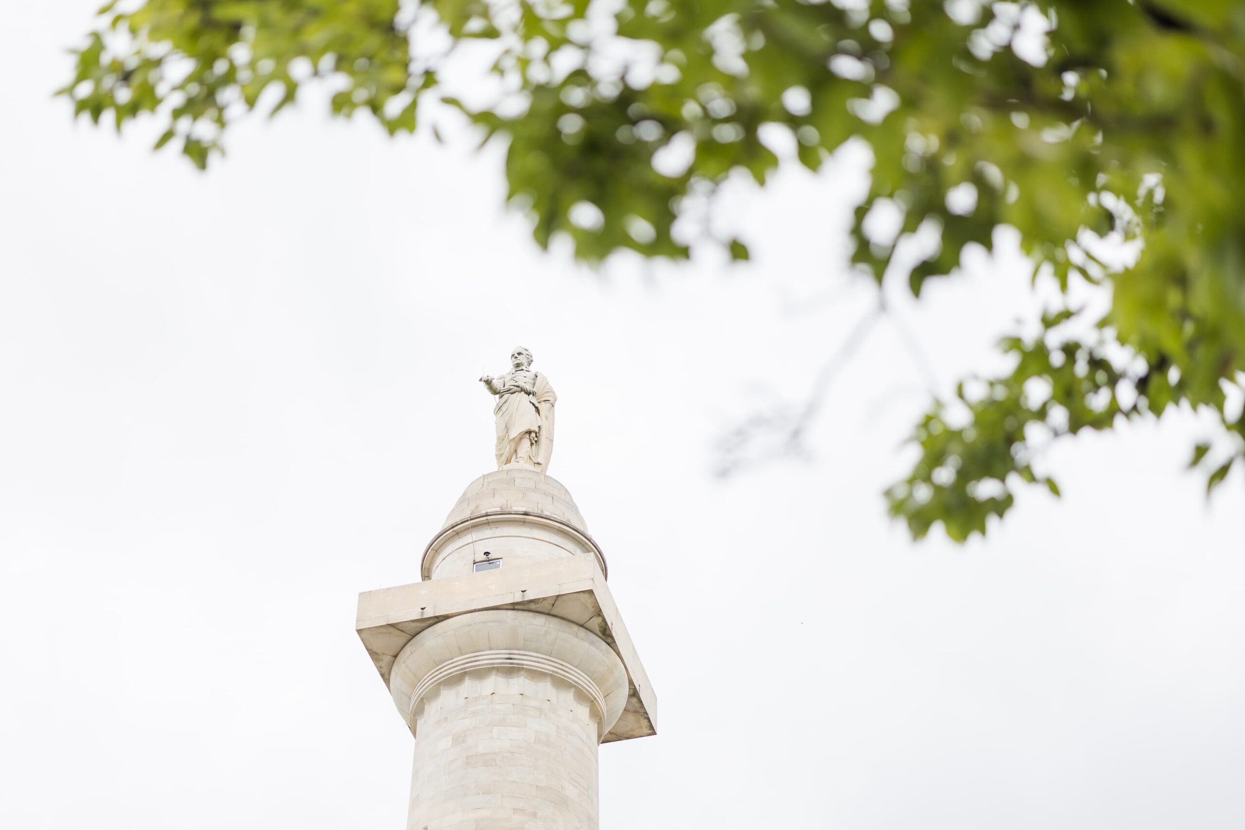 A large monument of George Washington sits high in the sky with green leaves in the foreground.