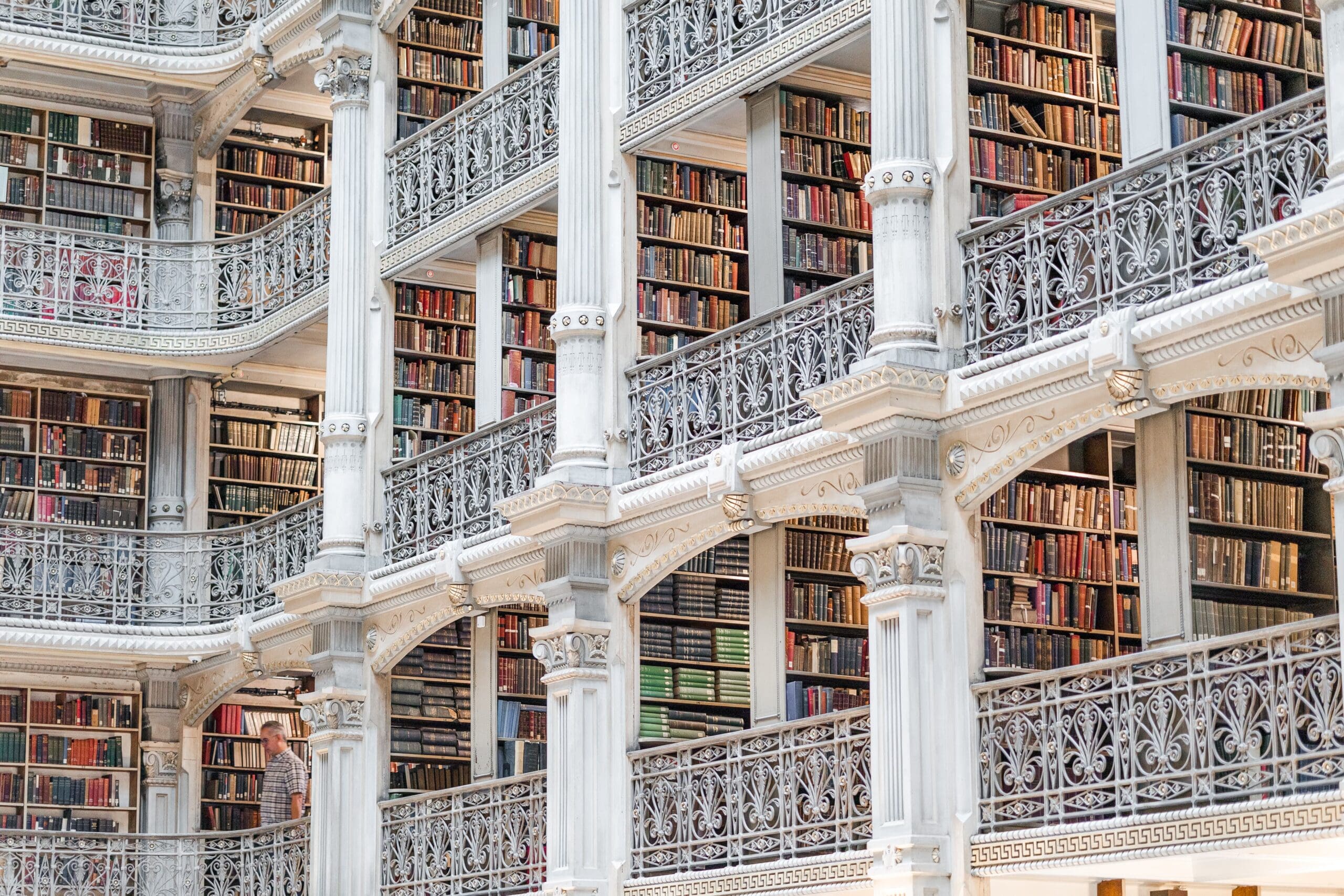 A grand library interior with four levels of book-filled balconies, adorned with ornate white railings and warm lighting, exuding a serene atmosphere.