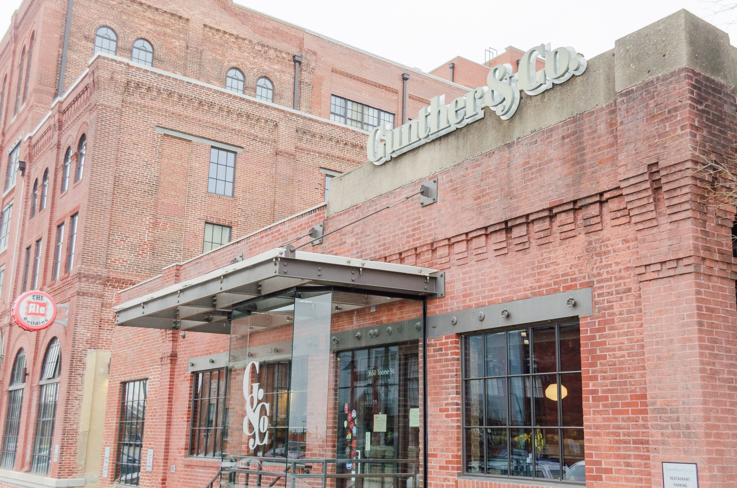 Red brick building with vintage industrial facade and large windows. Sign reads "Gunther & Co." Rustic and inviting atmosphere.