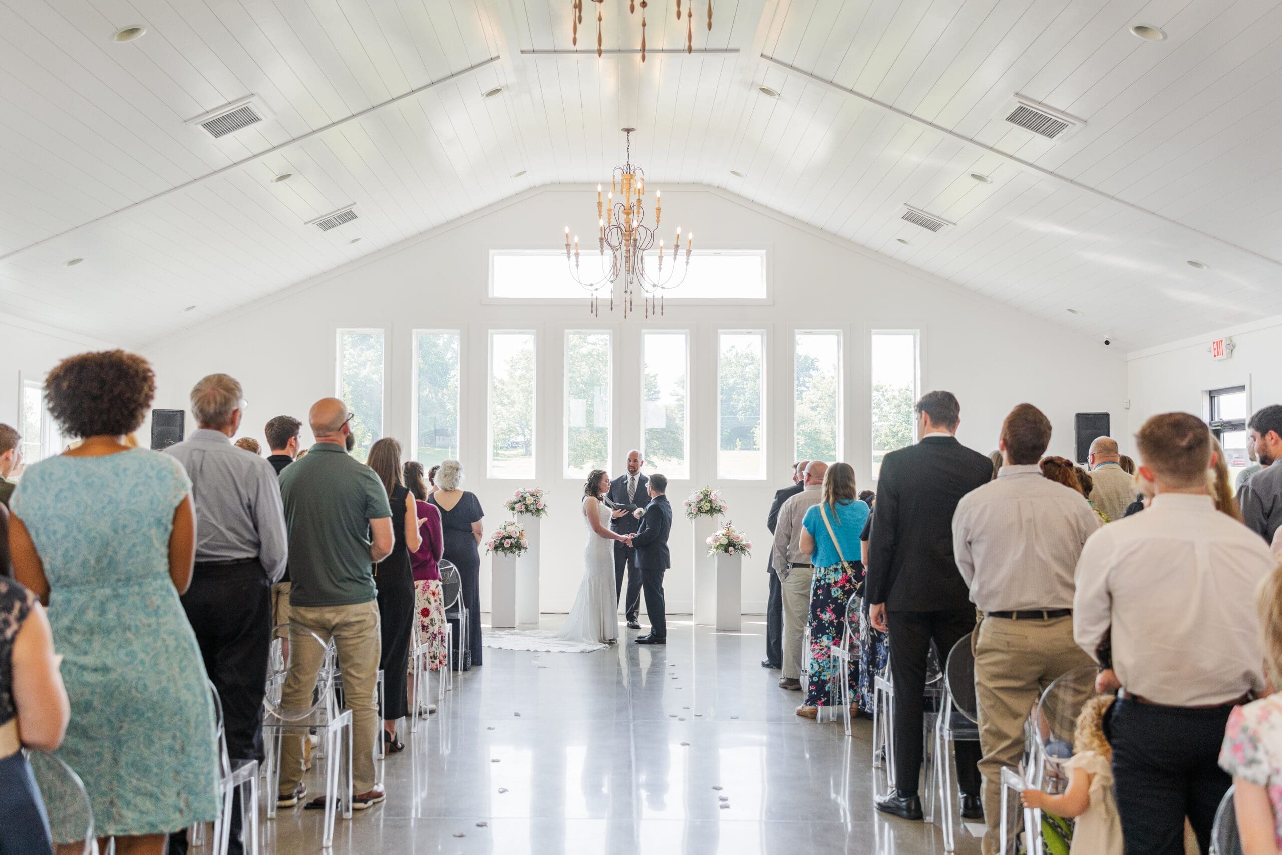 Wedding ceremony picturing the bride and groom facing each other at the altar while their guests stand at their seats facing them.
