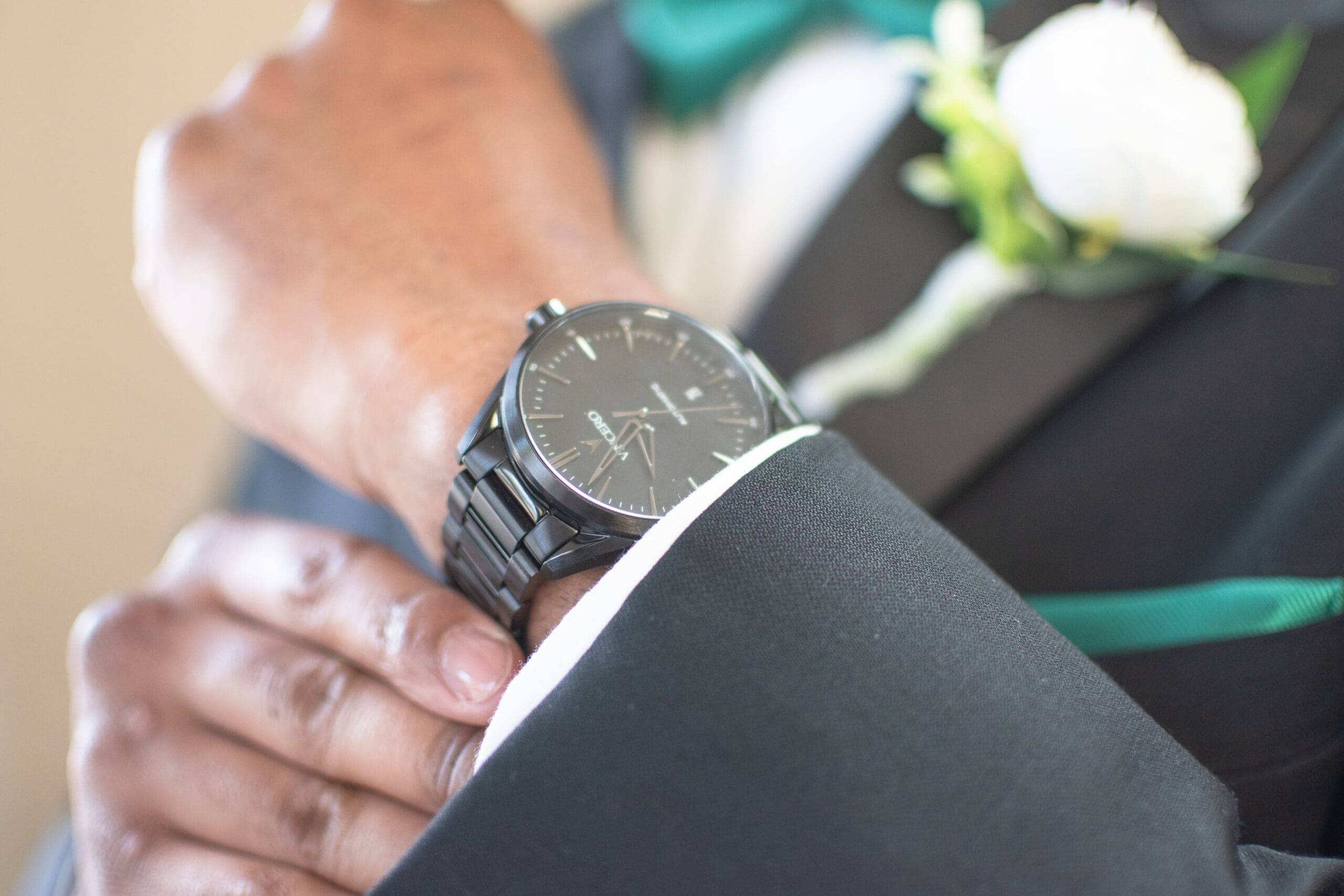 man holds his watch on his wrist in a black suit with green and white accents.