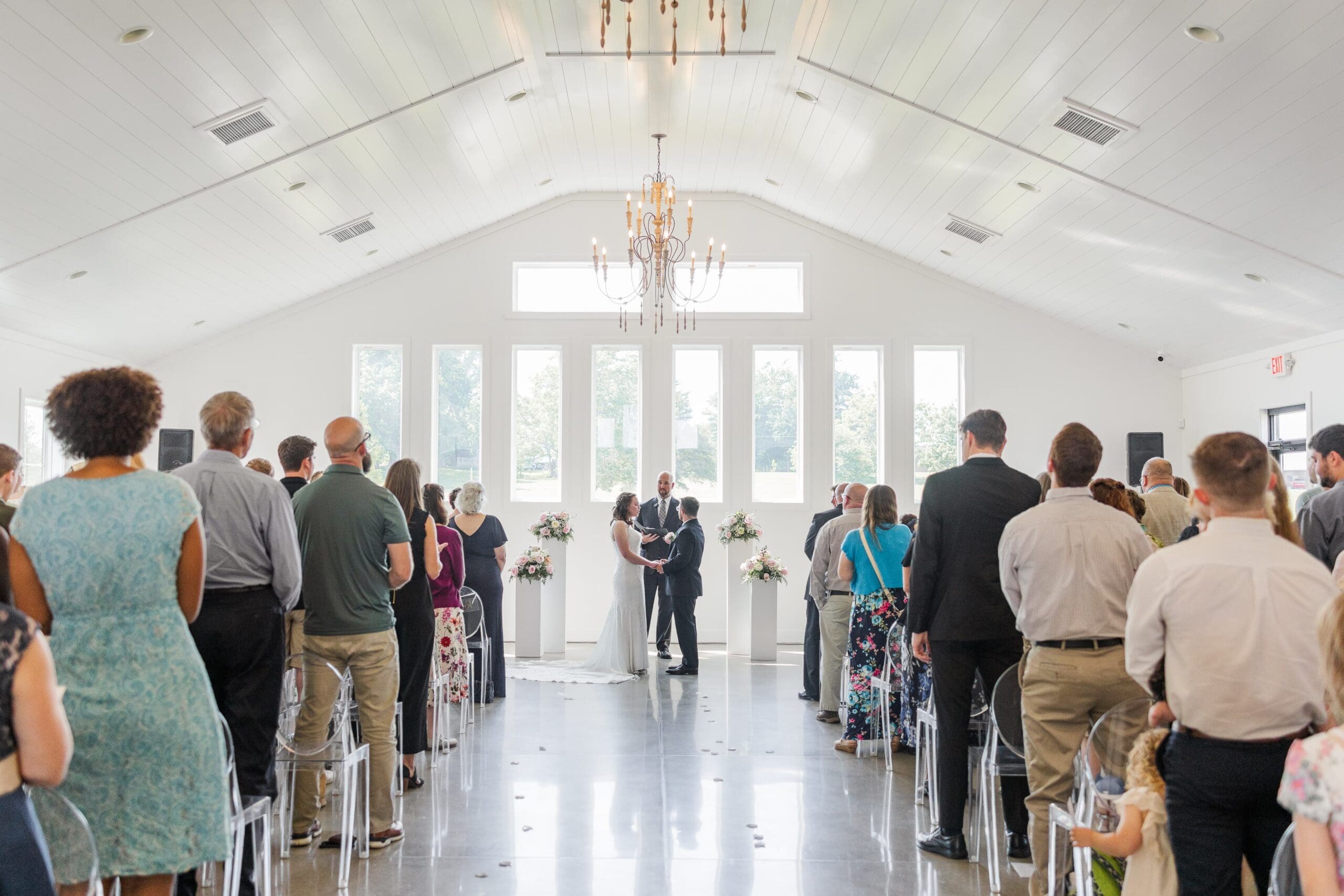 Wedding ceremony picturing the bride and groom facing each other at the altar while their guests stand at their seats facing them.