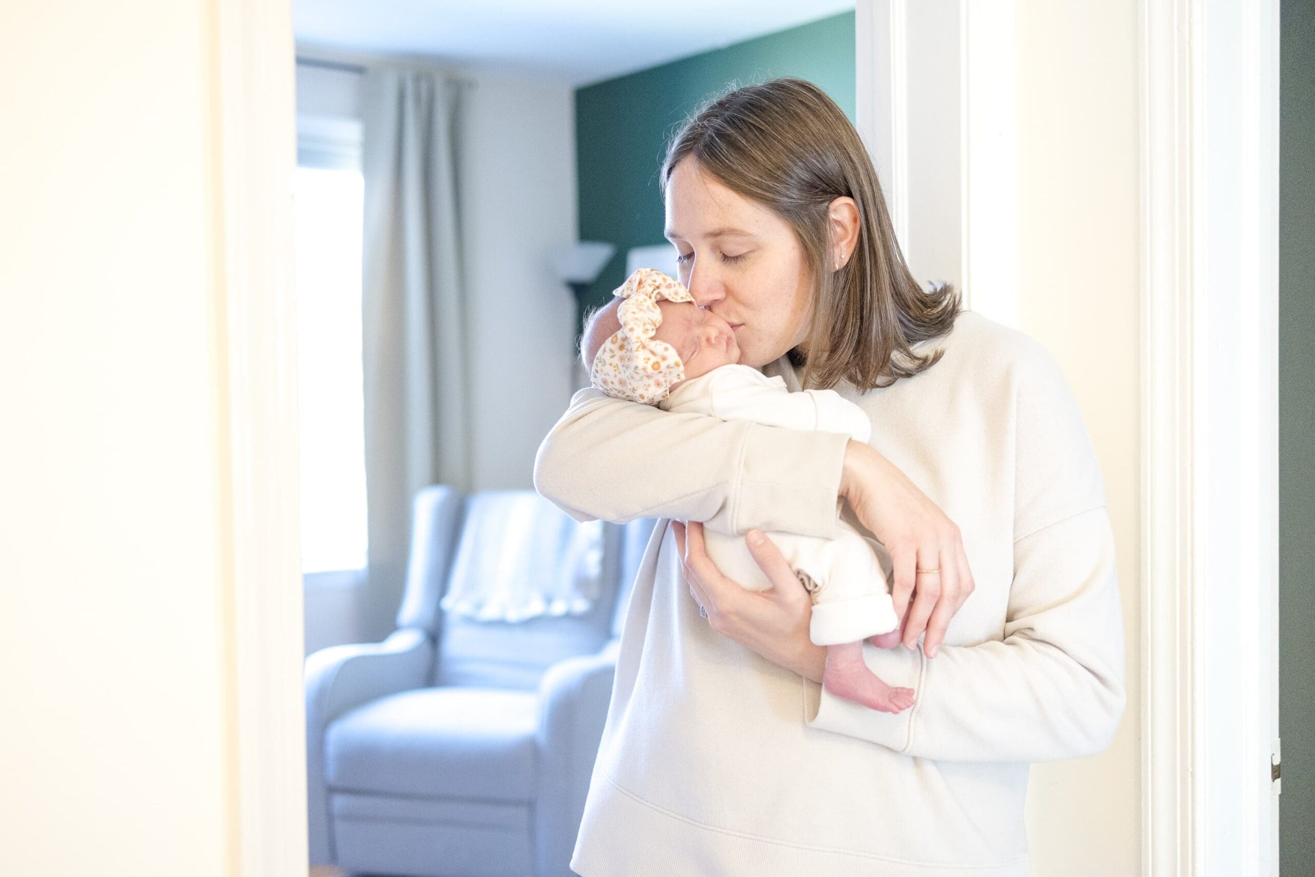 mom kissing her newborn baby as she holds her in front of a room in their house