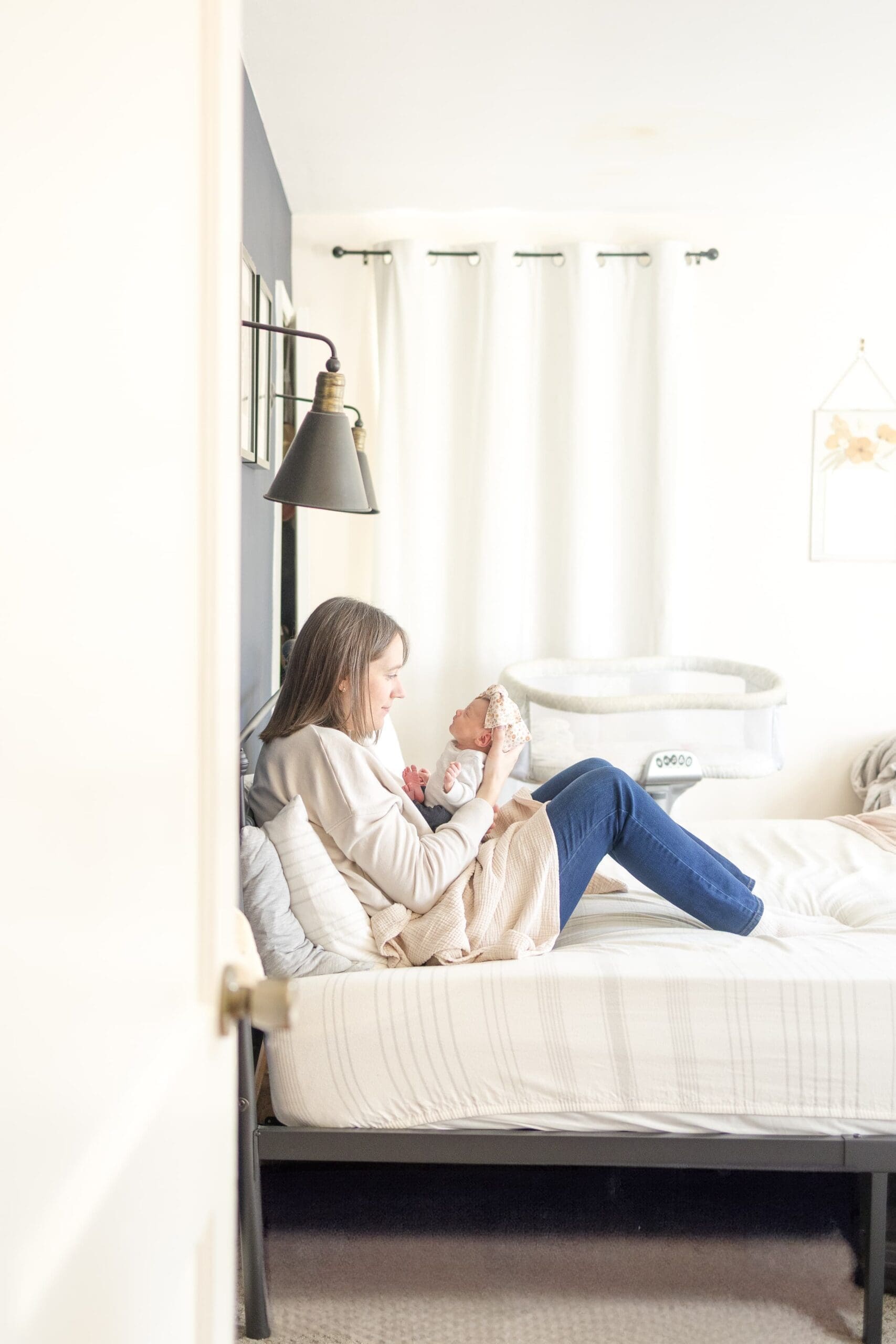 Mom cradling newborn in her bed. They are in a white bedroom with white sheets.