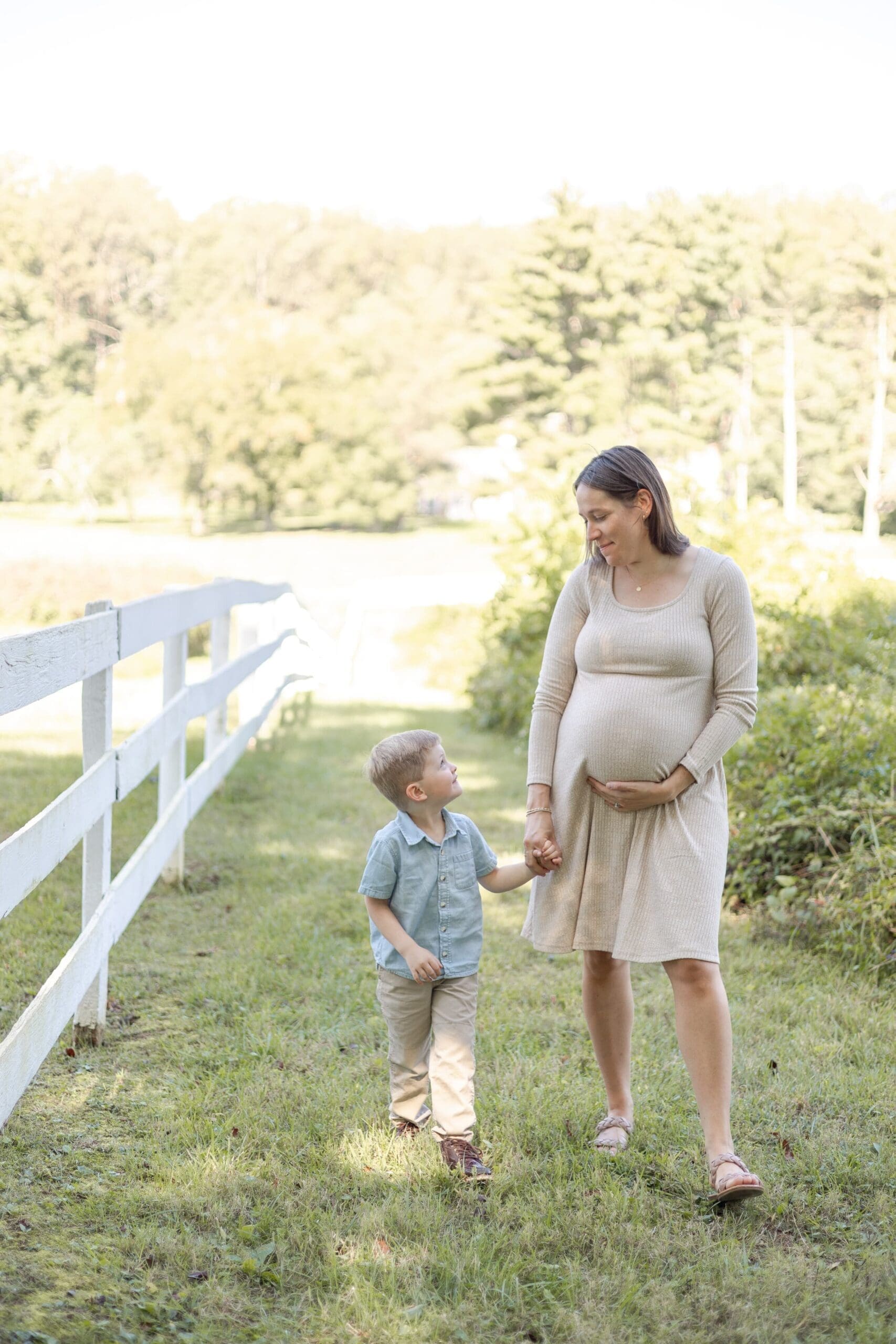 A couple stands close, the man gently placing his hand on the woman's pregnant belly. They are holding hands, conveying a sense of love and anticipation.