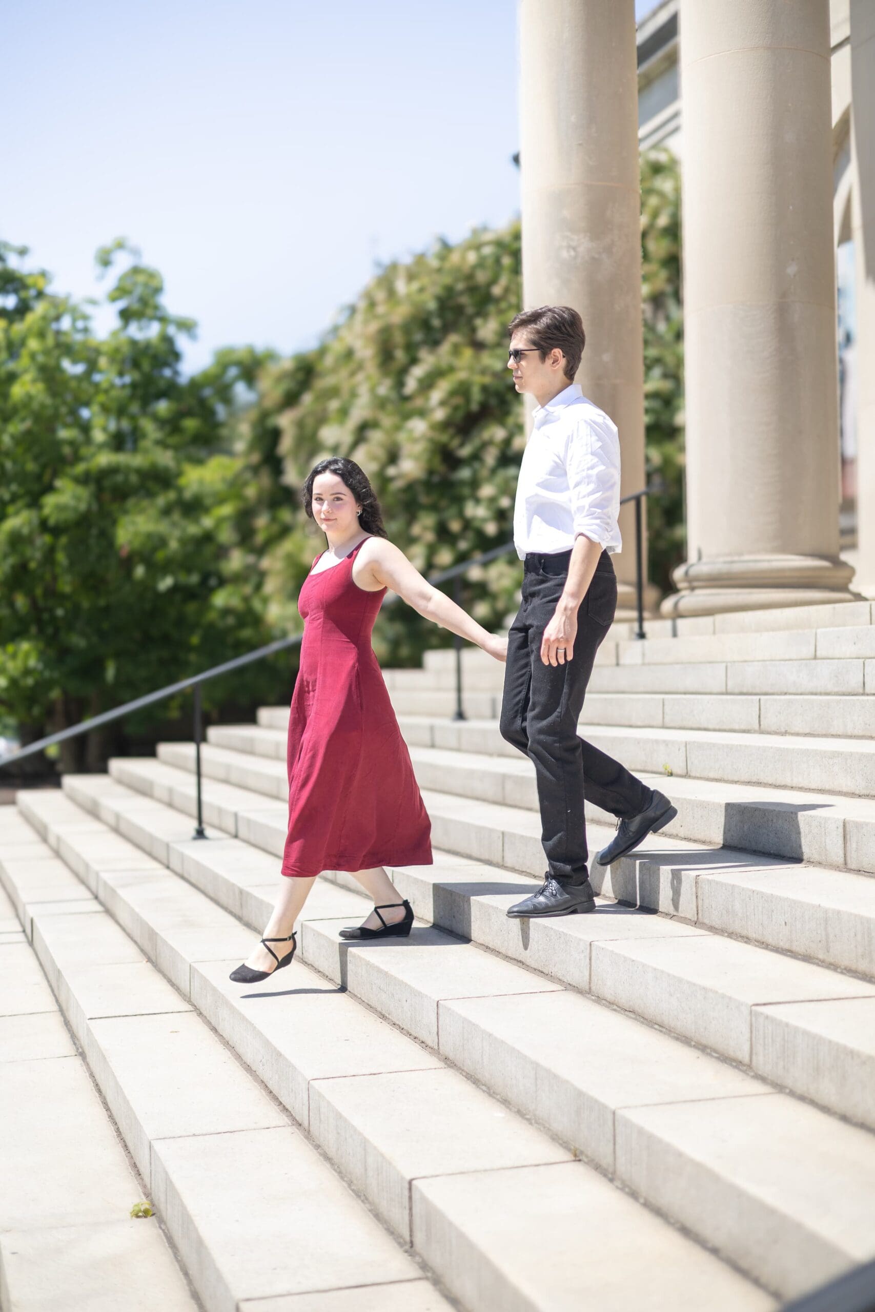 A couple holds hands outside the Baltimore Museum of Art. Stone pillars in the background as they walk down the front staircase. Photo taken by Lauren Beth Photos.