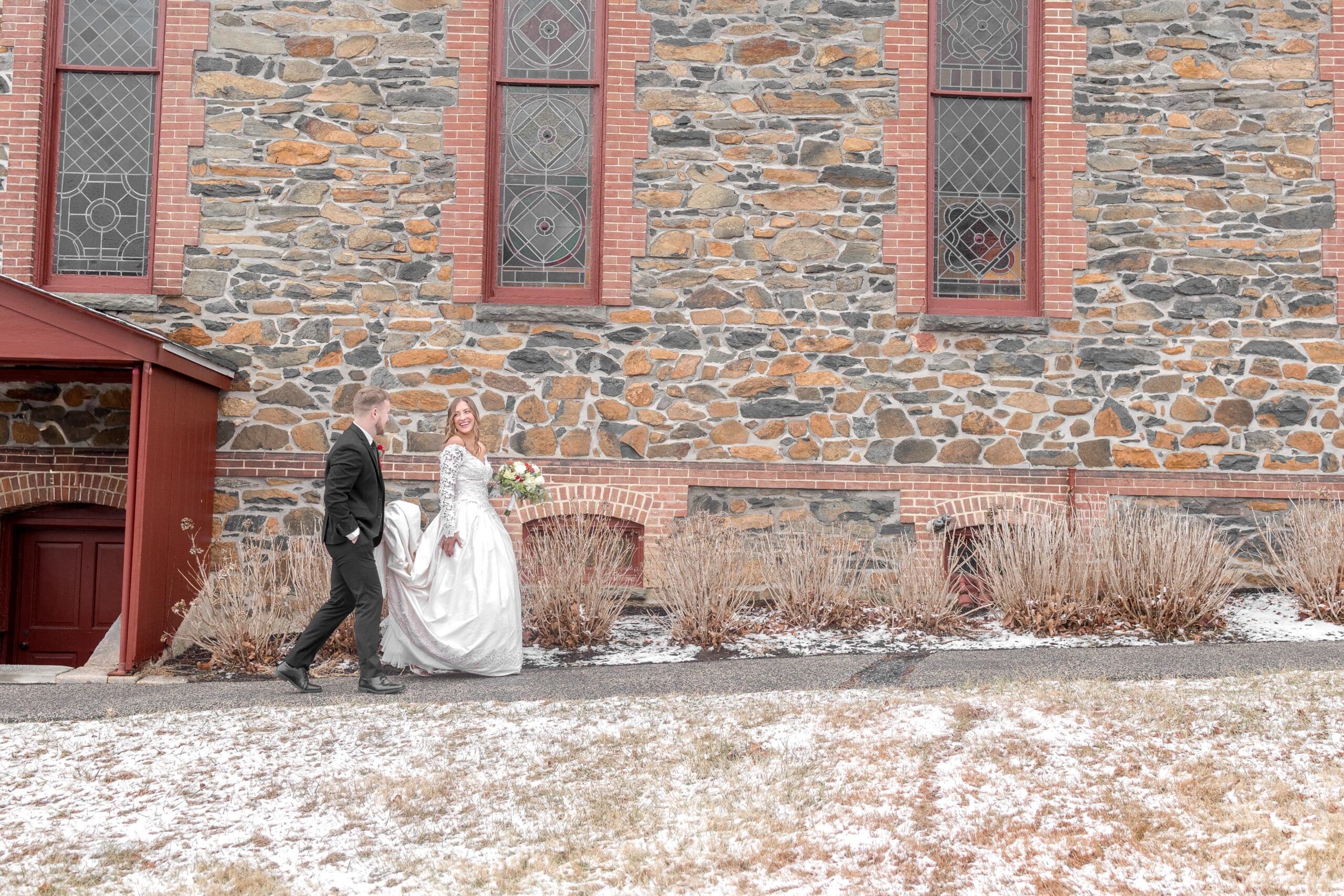 Beautiful bride in a white lace dress being guided down a black walkway by her husband in a black tuxedo out front of their ceremony building, a Catholic church.