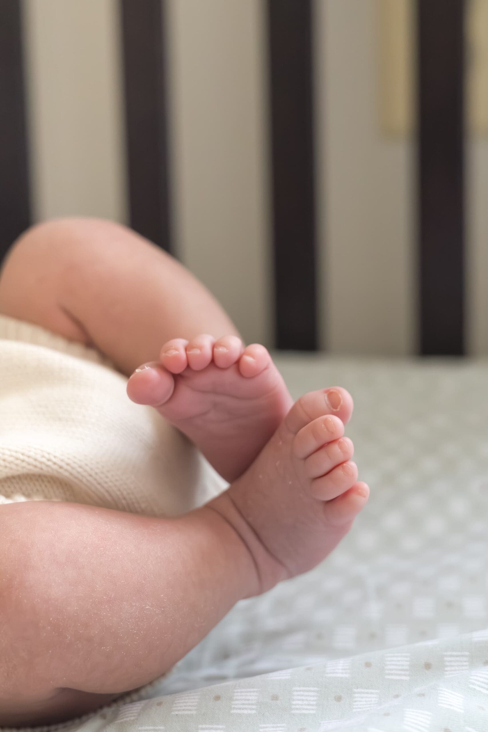 A baby's feet laying on a crib. The dark wooden crib has blue sheets.