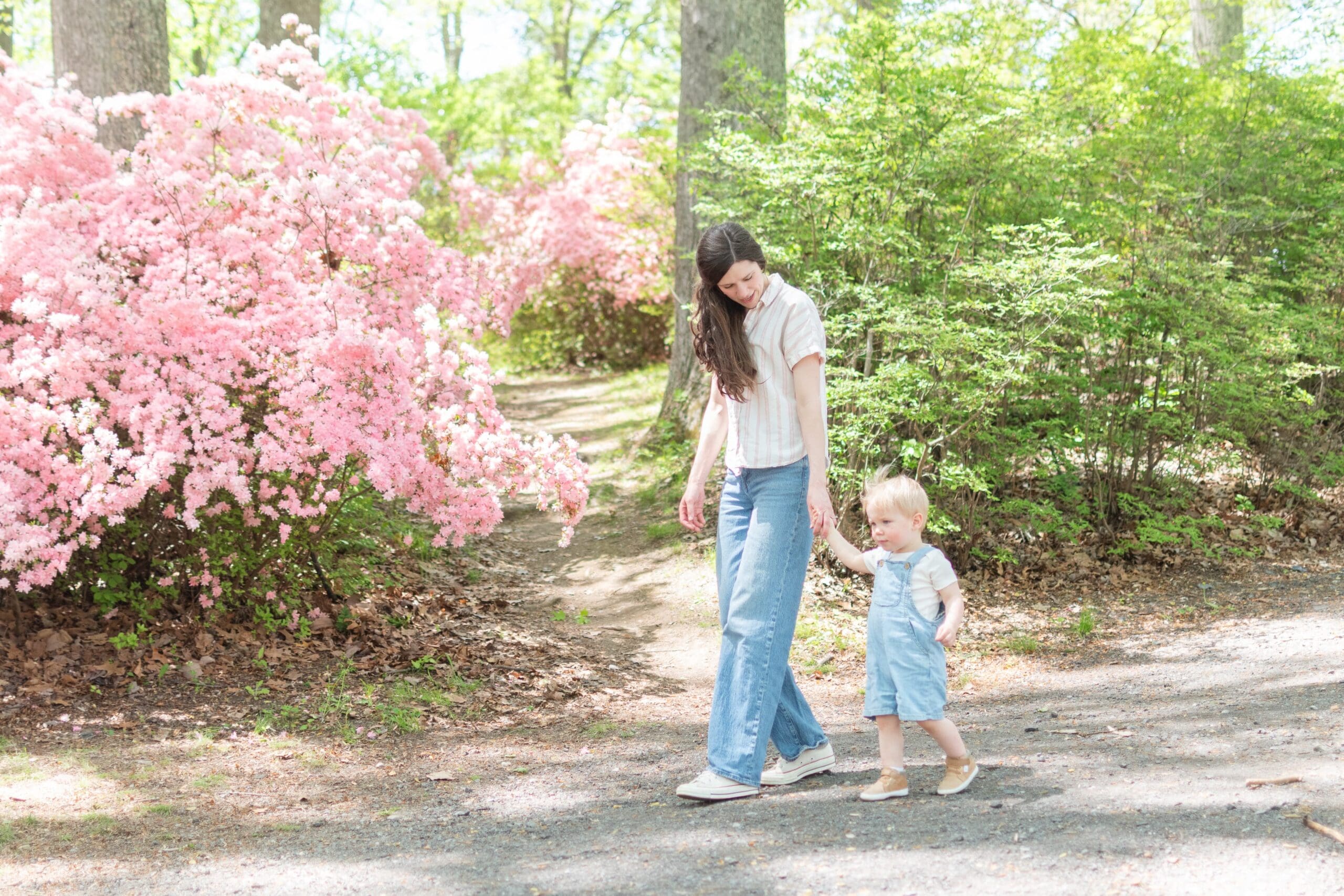A woman and one child walk closely together smiling at each other in front of vibrant pink flowers. The scene conveys warmth and family joy amidst nature.