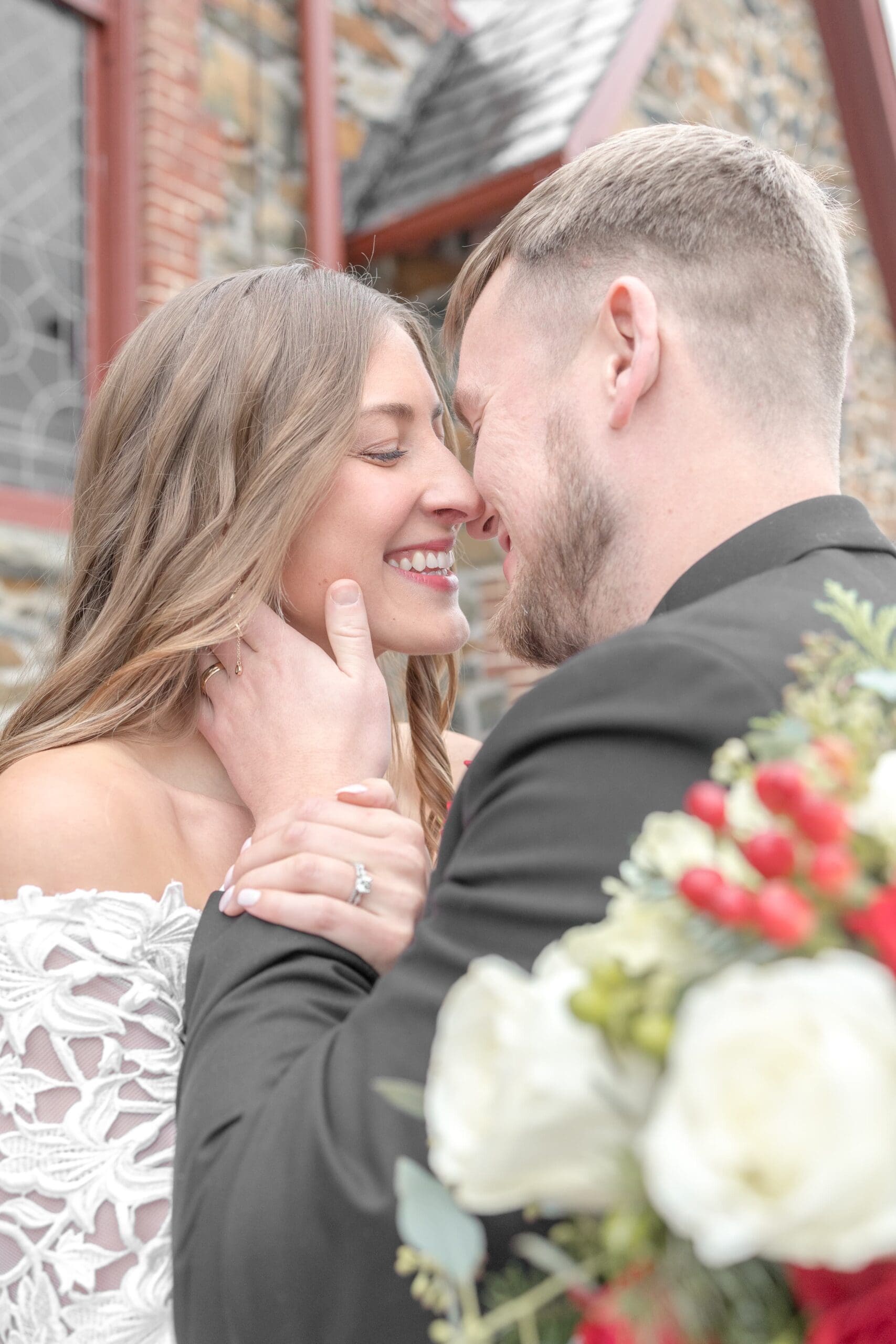 Beautiful bride smiling close to her new husband, nuzzling nose to nose, leaning in for a kiss with her bridal bouquet close by him.